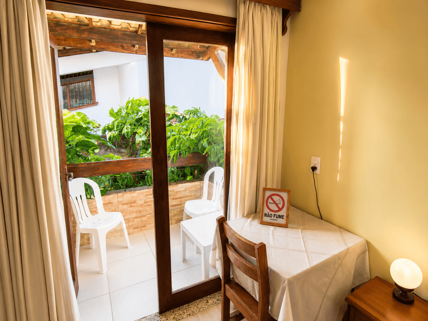 Quarto Lateral Duplo Standard da Pousada Poesia, com cama de casal, decoração aconchegante, mesa de apoio e acesso à varanda.